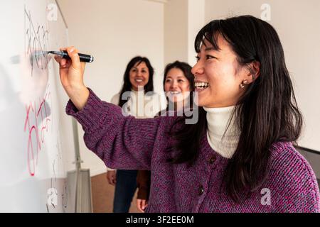 Adult Japanese lesson in a small classroom, with a teacher writing on a whiteboard while adult students watch and smile during an interactive language Stock Photo