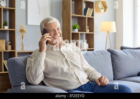 Happy senior man having phone conversation at home sitting comfortably on the sofa Stock Photo