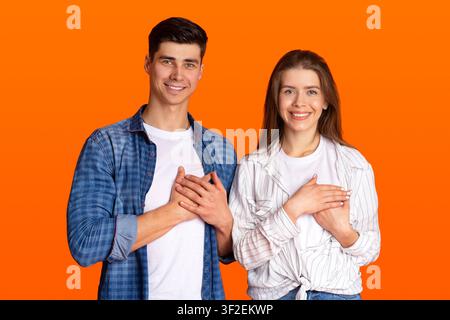Grateful gesture concept. Pretty smiling young male and female in casual clothes keep hands on chest, being thankful Stock Photo