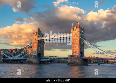 Tower Bridge Illuminated by Golden Sunset Under Dramatic Clouds Over River Thames in London England Stock Photo