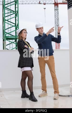 Architects and engineers discussing construction progress at a building site, wearing hard hats, planning next steps with a crane in the background, s Stock Photo