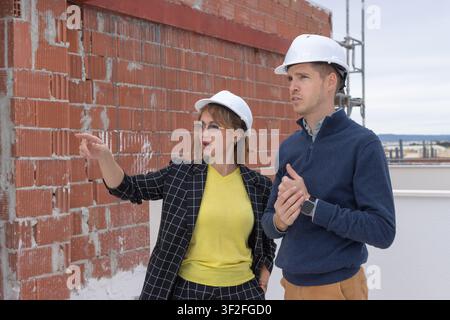 Two skilled architects or civil engineers, a woman pointing with her hand and a man listening intently, collaborating and planning on an unfinished bu Stock Photo