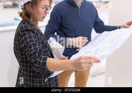 Architects or engineers in hard hats reviewing blueprints and floor plans, collaborating on ideas for a new residential or commercial real estate deve Stock Photo