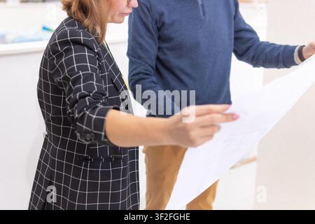 Business professionals analyzing blueprints, collaborating on a development project, discussing architecture plans, and planning a construction strate Stock Photo