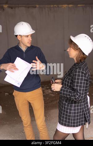 Construction site professionals discussing project plans, reviewing blueprints and progress, collaborating on building development, wearing protective Stock Photo