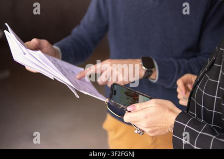 Professionals discussing project plans, analyzing paperwork and information on a smartphone, connecting traditional documents with digital data for st Stock Photo