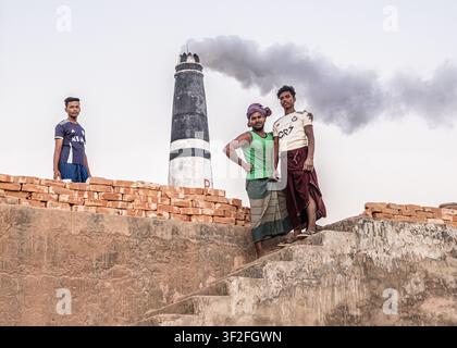 Chattogram, Bangladesh - 07 February 2026: View of three men standing near a brick kiln with a smoking chimney in the background. Stock Photo