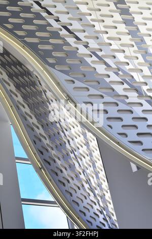 Abstract low-angle view of modern interior architecture featuring overlapping curved structures and perforated panels. Stock Photo