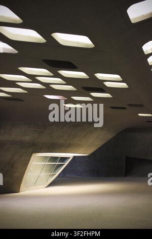 Interior of a modern building with exposed concrete surfaces, sloping walls and a ceiling of irregular rounded skylights casting soft daylight onto th Stock Photo
