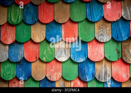 Full frame close-up background texture of rustic, rounded wooden shingles or roof shakes painted in alternating bright colors including blue, red, gre Stock Photo
