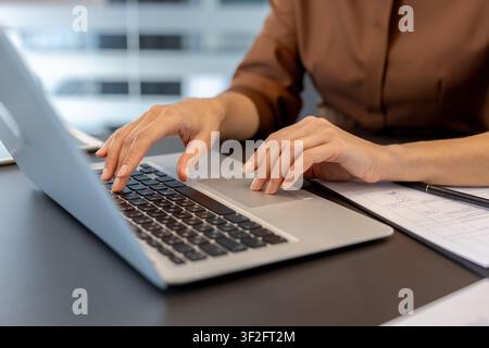 Person's hands busily engaging with a silver laptop keyboard and trackpad, performing data entry, communicating, and managing tasks on a contemporary Stock Photo