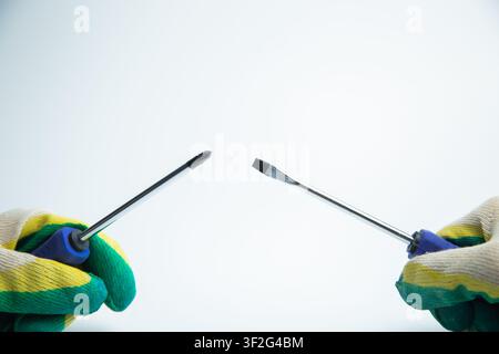 Close-up of two hands in work gloves holding screwdrivers against a white background. Concept of Stock Photo