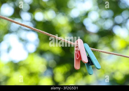 Pastel colored plastic clothespins hanging on a rope clothesline with a blurred green nature background Stock Photo