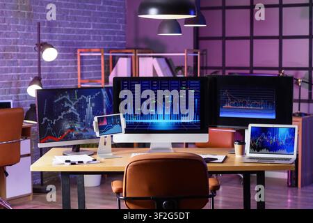 Empty modern office desk with multiple computer monitors displaying financial stock market data and charts, the workspace is equipped for trading and Stock Photo