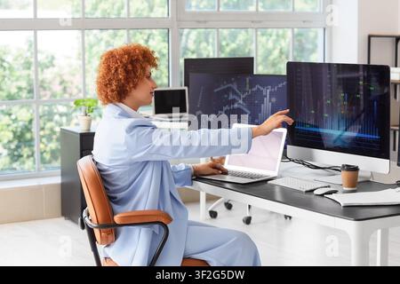 Female trader analyzing financial data on multiple computer screens in a modern office environment Stock Photo