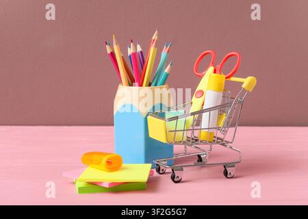 Colorful school supplies and stationery in a miniature shopping cart and pencil holder on a pink wooden table Stock Photo