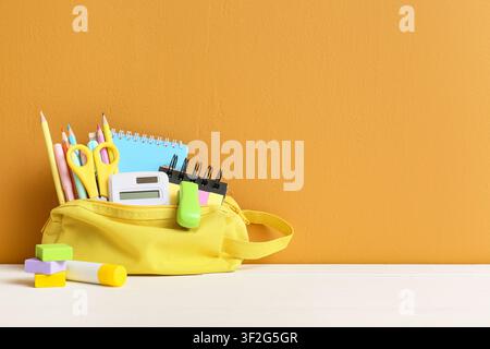 Yellow pencil case filled with school supplies back to school concept education and learning on a white table with orange background Stock Photo