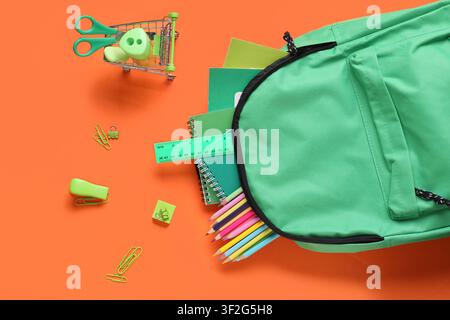 Green backpack with school supplies and stationery on an orange background, back to school and education Stock Photo