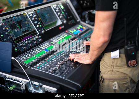 Close-up of an audio engineer adjusting a professional digital mixing console during a live music performance at an outdoor concert venue. Stock Photo