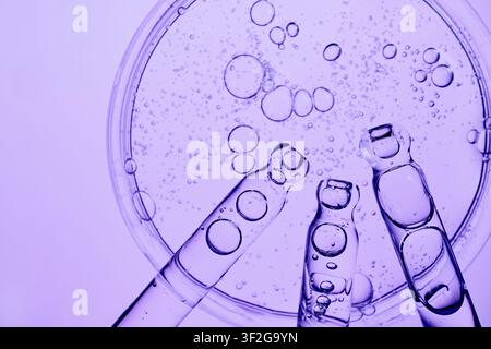 Droppers dispensing purple liquid into petri dish creating various bubbles Stock Photo