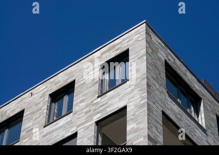 Low angle view of a contemporary office or residential building corner featuring an elegant grey stone tile cladding facade and dark window frames. Stock Photo