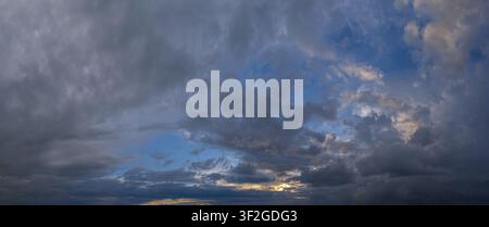 A breathtaking sunset scene with a mix of dark clouds and patches of bright orange light breaking through, creating a striking contrast against the de Stock Photo