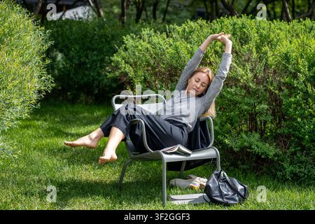 Relaxed woman dozing napping, sitting on folding chair on lawn in nature park outside outdoors Stock Photo