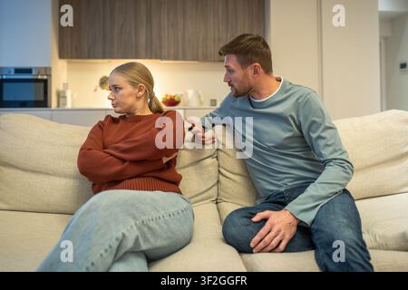 Manipulative dishonest male partner sitting on couch discussing and justifying lies with angry wife Stock Photo