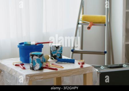 Home Renovation Tools Prepared for Painting with paint cans, brush, roller and ladder prepared for apartment improvement, wall painting, maintenance and interior repair. Stock Photo