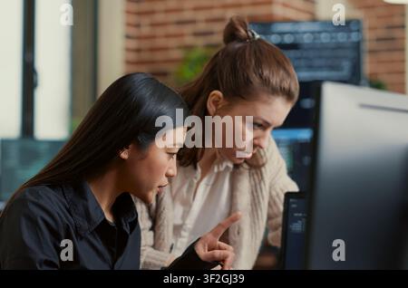 Software Engineers Discussing Source Code on Laptop in a software development office, showing programmers collaborating on source code, algorithms and data coding workflow. Stock Photo