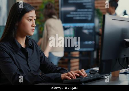 Programmer Compiling Algorithm with Team Behind in a software development office, showing programmers collaborating on source code, algorithms and data coding workflow. Stock Photo