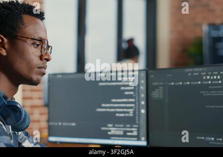 Software Developer Adjusting Glasses While Coding in a software development office, showing programmers collaborating on source code, algorithms and data coding workflow. Stock Photo