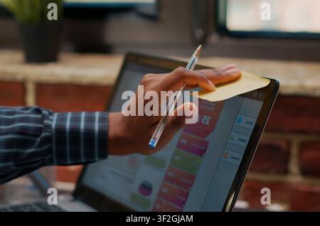 Employee Placing Reminder Notes on Laptop Screen in a company office, using adhesive notes on a laptop screen to organize schedule, presentation tasks and reminders. Stock Photo
