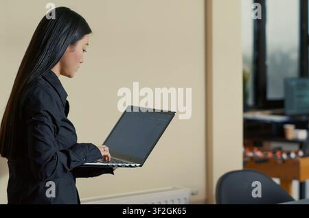 Asian software developer sits down with a laptop coding interface in a cybersecurity agency, preparing to write code beside a colleague. Stock Photo