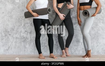 Fit women in sportswear standing with fitness mats in hands near wall Stock Photo