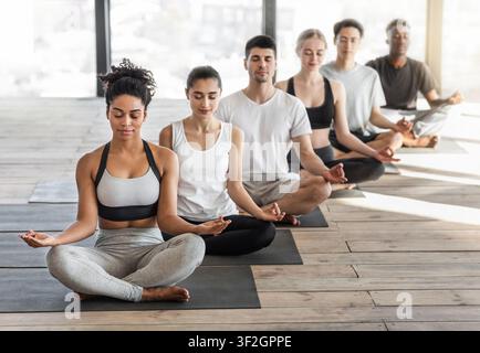 Meditation Class. Group Of Fit Young People Practicing Yoga In Light Studio Stock Photo