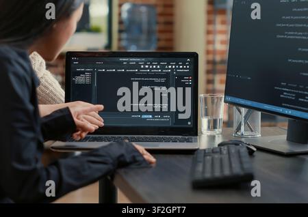 Programming team reviews an algorithm on a laptop screen, pointing at source code while collaborating on a data coding project at the desk. Stock Photo