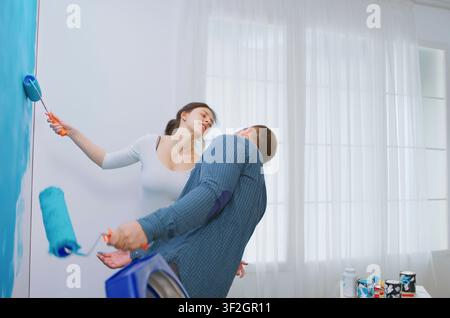 Cheerful young couple dances while decorating an apartment and painting walls, turning home renovation, repair and interior improvement into a fun activity. Stock Photo