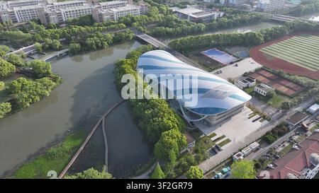 An early morning aerial view highlights a striking modern indoor sports arena with a distinctive organic shell-shaped roof of blue and white curved pa Stock Photo