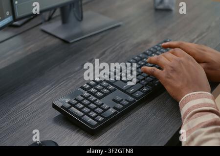 African American programmer types on a keyboard while viewing programming interfaces on multiple screens, developing algorithms as a system engineer at a desk. Stock Photo