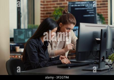 Coworkers compare source code on a laptop and computer monitor in an IT development office, collaborating on data coding and a group software project. Stock Photo