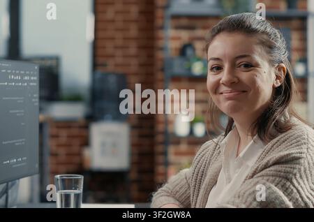 Focused portrait with software developer typing programming language on computer keyboard turning head and smiling at camera around computer screens, showing developer teamwork, source code. Stock Photo