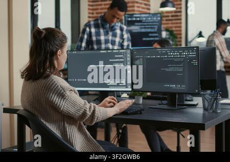 Concentrated software developer coding software reviewing multiple computer screens around computer screens, showing developer teamwork, source code discussion and cloud programming workflow. Stock Photo