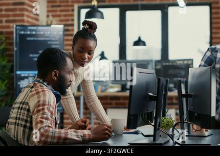 Collaborative team reviews cloud interface code around computer screens, showing developer teamwork, source code discussion and cloud programming workflow. Stock Photo