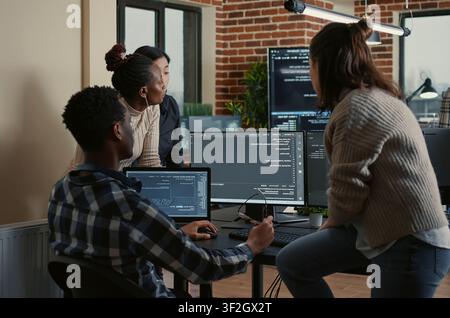 Software developers discuss cloud programming innovation as the rest of the team joins, collaborating on big data and server room computing. Stock Photo