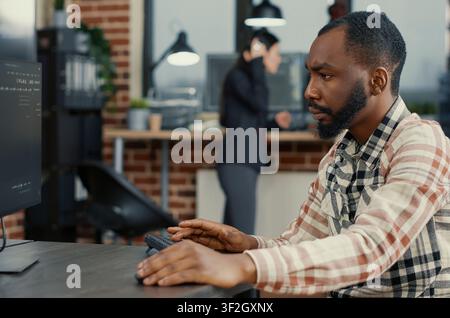 Static portrait of african american system engineer working concentrated reviewing computer screen around computer screens, showing developer teamwork, source code discussion and cloud programming. Stock Photo