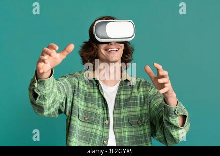 Young guy in virtual reality headset playing computer games on turquoise background Stock Photo