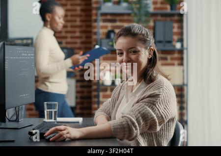 Programmer types source code on a computer keyboard, turning with a confident smile while working on software development in a technology office. Stock Photo
