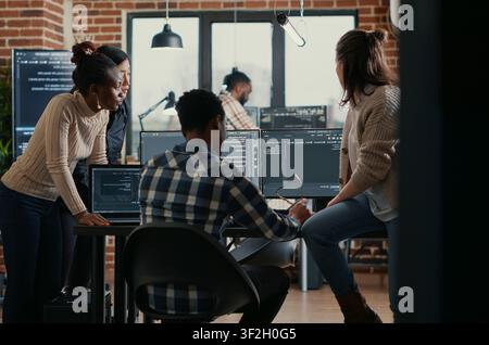Software programmers discussing about online cloud computing while the rest of the team joins in front of multiple screens compiling code, coders doing teamwork looking at running algorithms. Stock Photo
