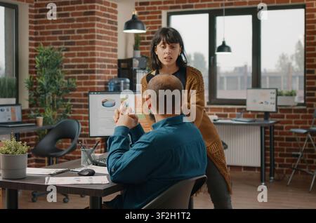 Colleagues working together on business project, talking about marketing strategy at desk, workmates brainstorming ideas to design rate charts on computer to plan data analysis. Stock Photo